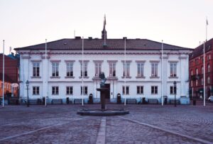Vit kommunbyggnad med fontän på ett kullerstensbelagt torg